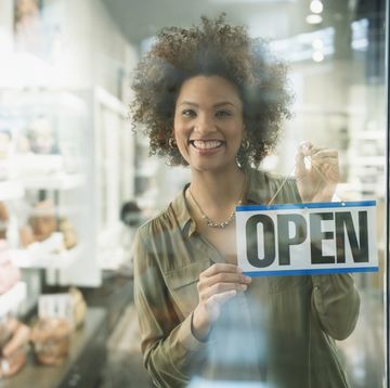 black woman holding open sign in store window