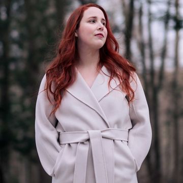 dylan farrow stands in a yard with tall trees behind her