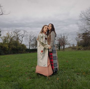 Two sisters stand in a grassy field with a body of water in the background two sisters stand in a grassy field with a body of water in the background