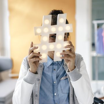 young woman hiding behind hashtag sign in studio